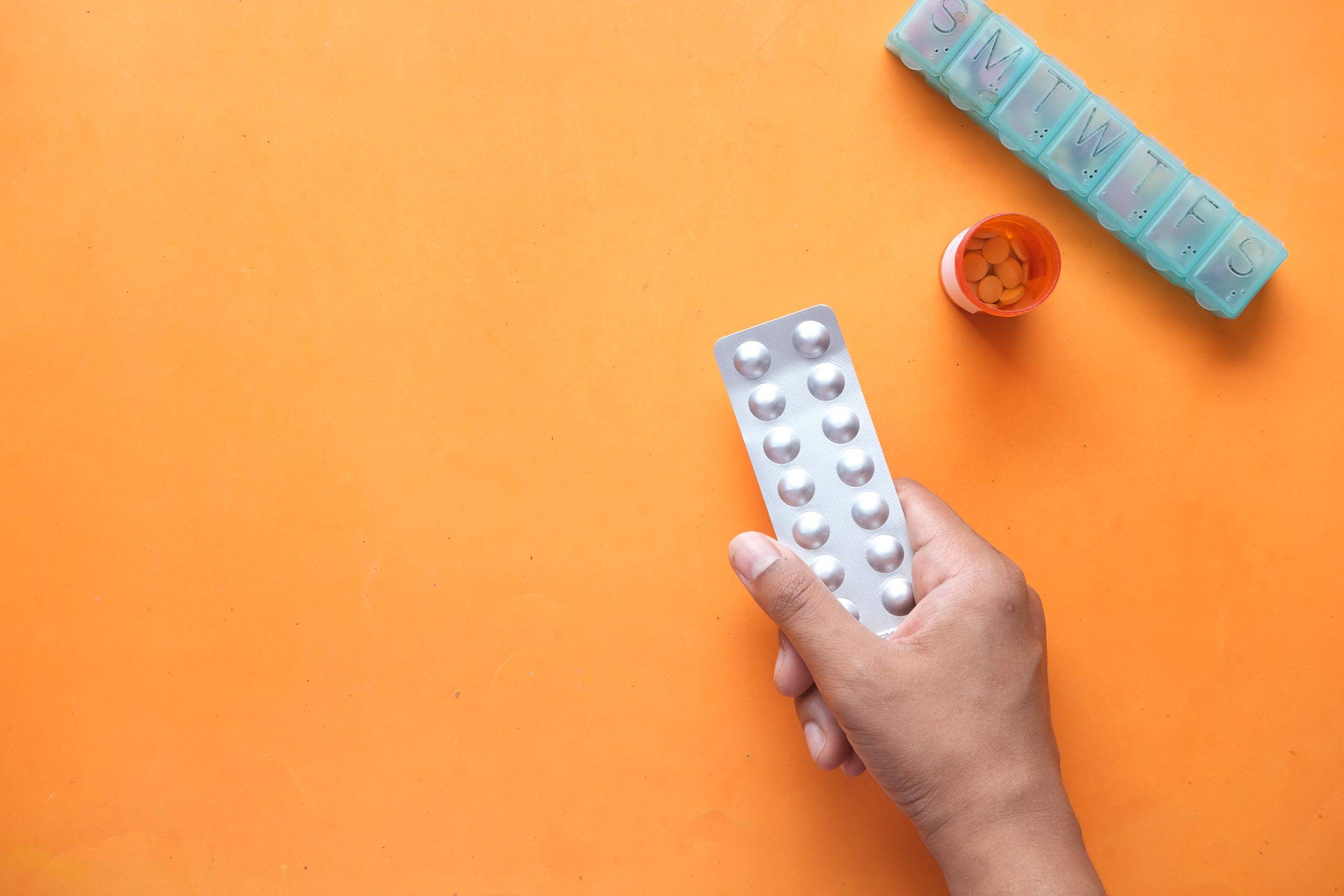 orange-background-hand-holding-birth-control-pills